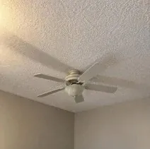 Textured bedroom ceiling repainted white around a ceiling fan